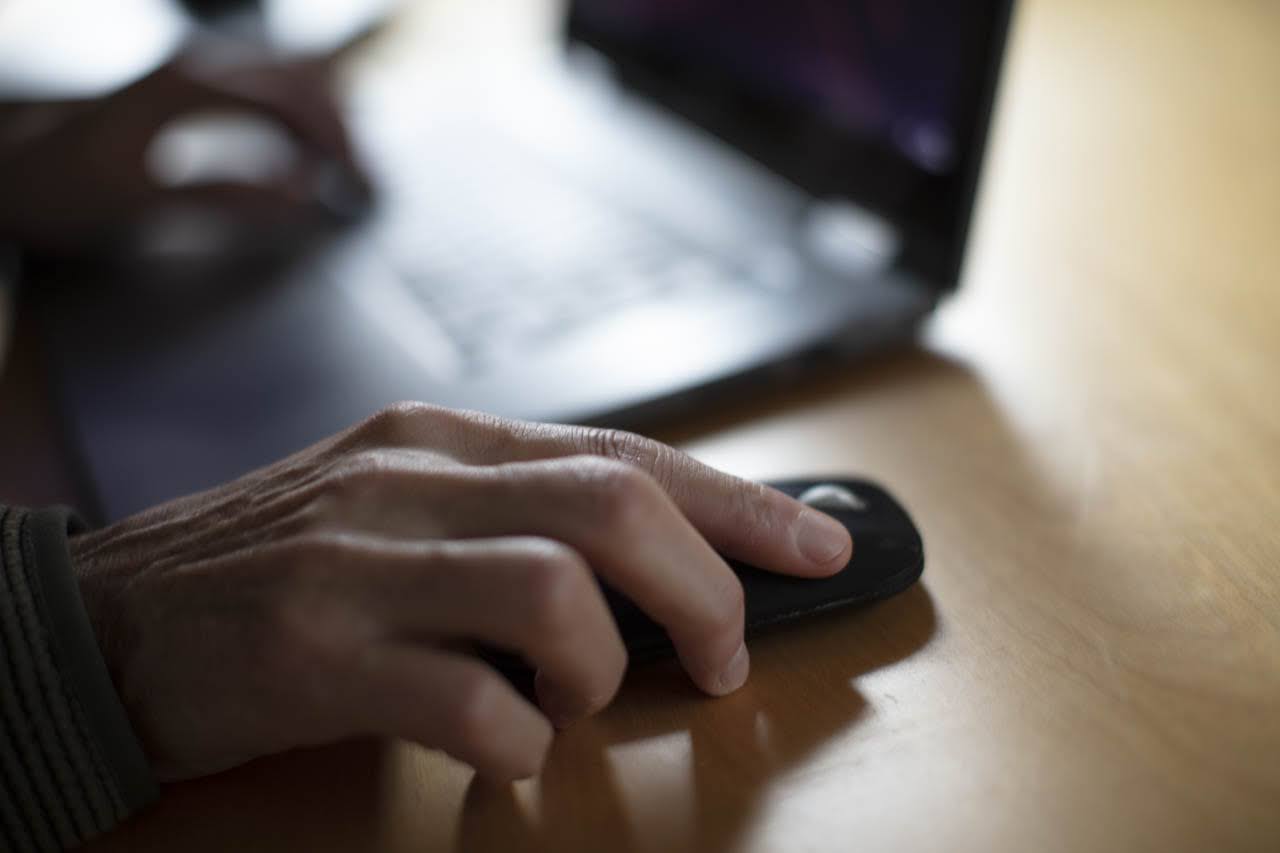 Mano su un mouse con laptop sullo sfondo